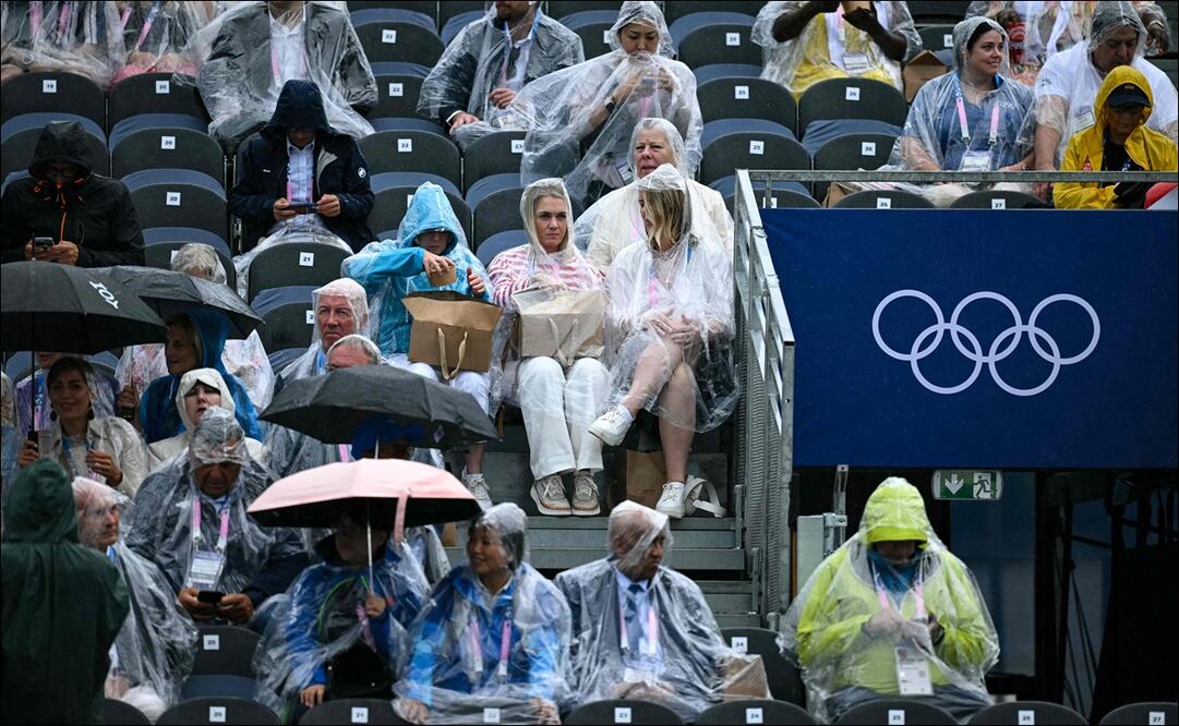 Aficionados portan sus sombrillas e impermeables para protegerse de la lluvia, previo al inicio de la ceremonia de inauguración de los JO. FOTO: AFP